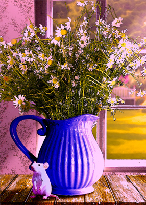 Small white mouse sitting next to a blue vase containing chamomile.
